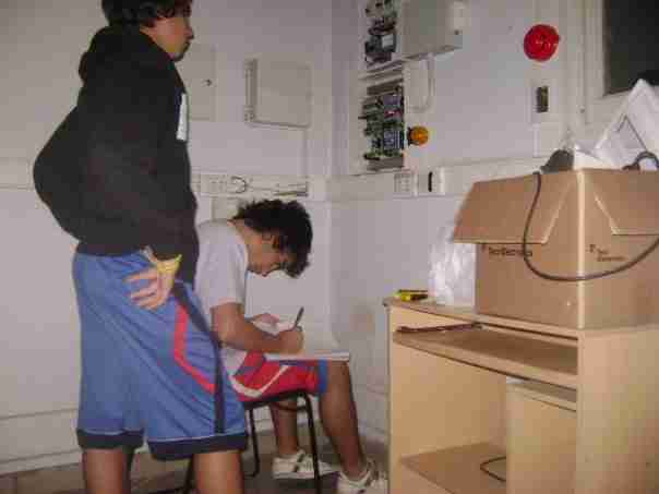 Technicians working on security systems. There is an electronic access control panel and a security alarm panel open being fixed.