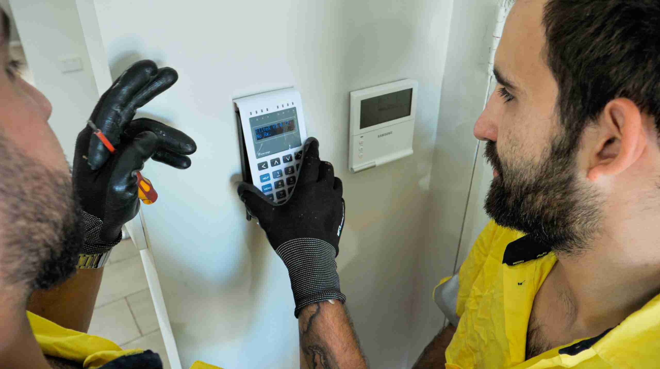 Technicians assessing fault on Electronic Access Control Keypad wearing safety gloves and using a screw driver.